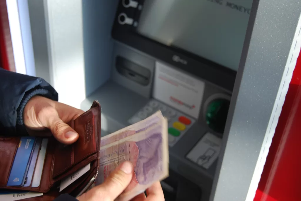 A person collects cash from a cash machine holding British Pounds. : Photo by Nick Pampoukidis on Unsplash https://unsplash.com/license
