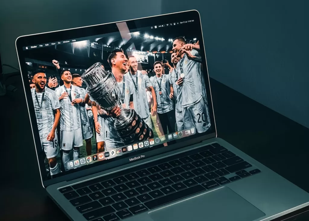 Glossy, digitally-enhanced images of sport victories often hide a sad truth of the countries hosting such events. : ‘Messi on laptop’ by Zesan H is available at https://tinyurl.com/2cwujx5v Licence by Unsplash