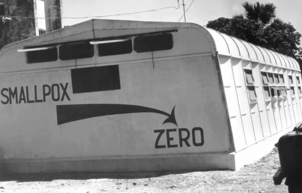 A sign displaying the WHO’s goal of eradicating smallpox on the side of a clinic annex in East Pakistan (modern-day Bangladesh) in 1966. : Centers for Disease Control and Prevention Public domain
